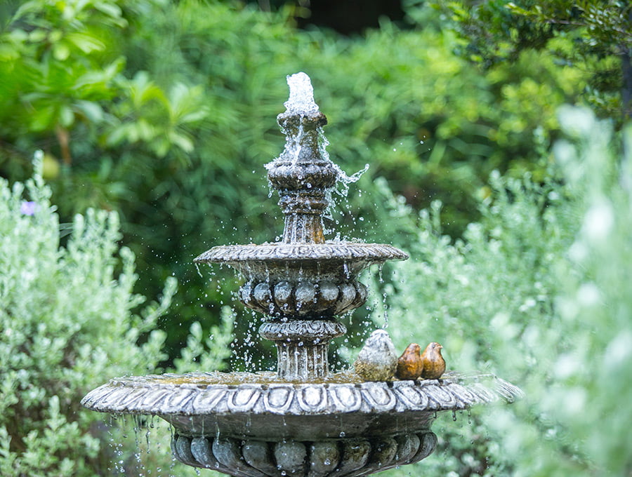 Una bonita fuente de piedra natural colocada en un hermoso jardín. Tiene además unos pájaros de piedra como adorno de la fuente de agua.