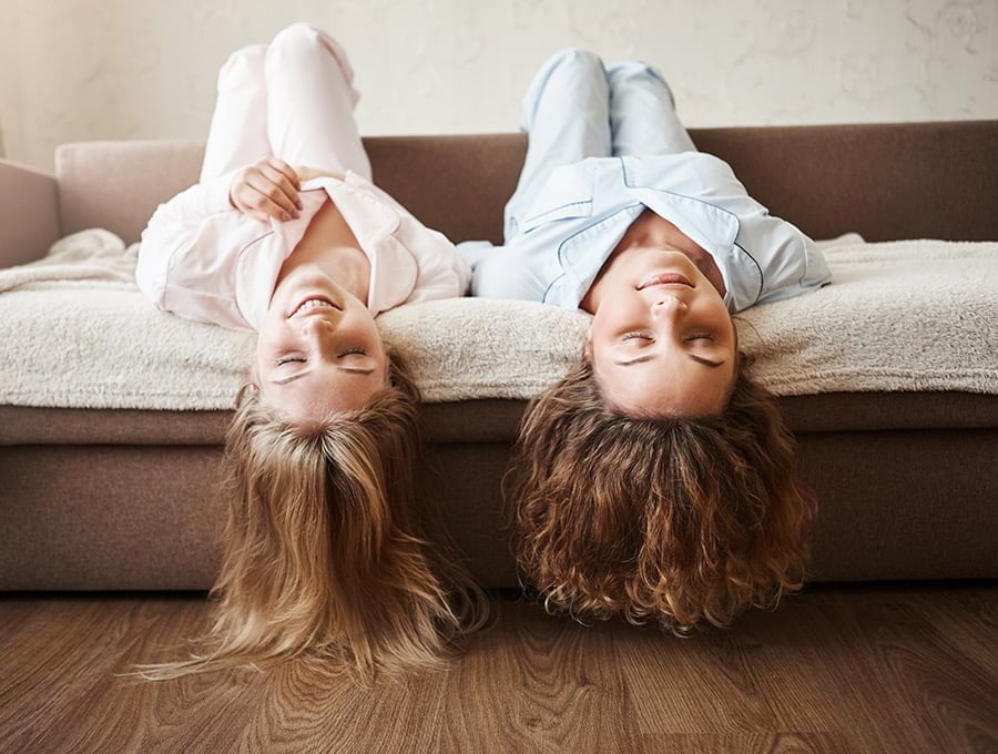 Dos niñas en pijama tumbadas boca arriba en el sofá cama. Tienen la cabeza por fuera, diría que están jugando.