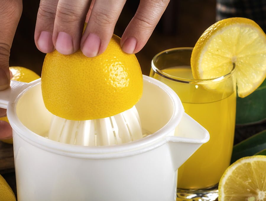 Esta persona está exprimiendo algunos limones en un exprimidor de plástico. Está haciendo zumo de limón para tomar. Hay un vaso lleno de zumo, justamente al lado.