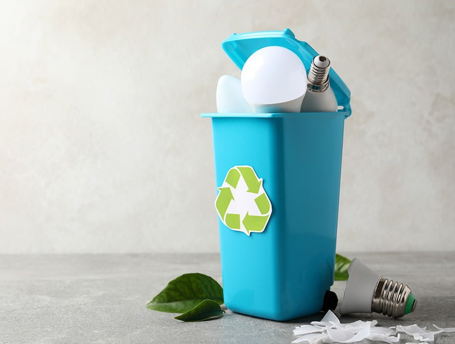 Varias bombillas rotas y fundidas dentro de un cubo de basura de plástico de color celeste. Tiene el logo de reciclaje.