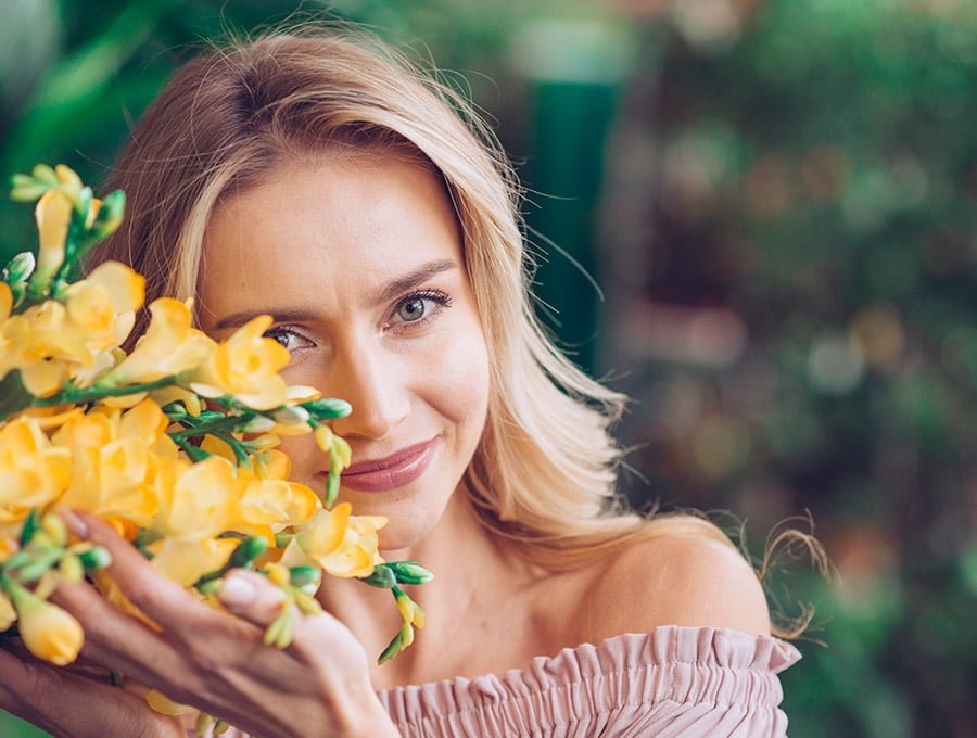 Esta mujer está tocando con sus manos una planta llena de flores de fresias amarillas.